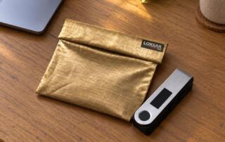 SHIELDSAK Faraday pouch beside a stick-style hardware wallet on a desk